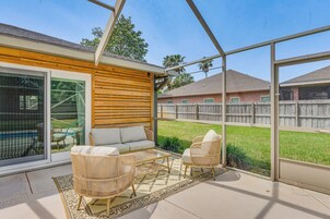 Un patio cubierto con mobiliario de mimbre, una puerta de vidrio que da al exterior y vistas a un jardín trasero con cerca de madera.