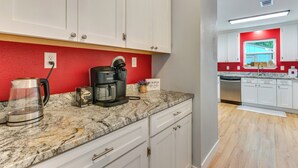 A modern kitchen with white cabinets, a red accent wall, a coffee maker, and a dishwasher. - Pool Days! Family Getaway Near Pensacola Beach (Gulf Breeze)
