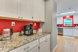 Una cocina moderna con armarios blancos, una pared de acento roja, una cafetera y un lavavajillas.