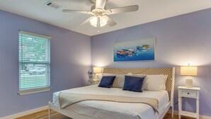 A bedroom with a bed, a ceiling fan, a painting, and a nightstand with a lamp. - Pool Days! Family Getaway Near Pensacola Beach (Gulf Breeze)