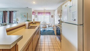 A compact kitchen with a refrigerator, sink, and dining area. - Lake-view Balcony, Pool Access! Sunset Beach Condo (Sunset Beach)