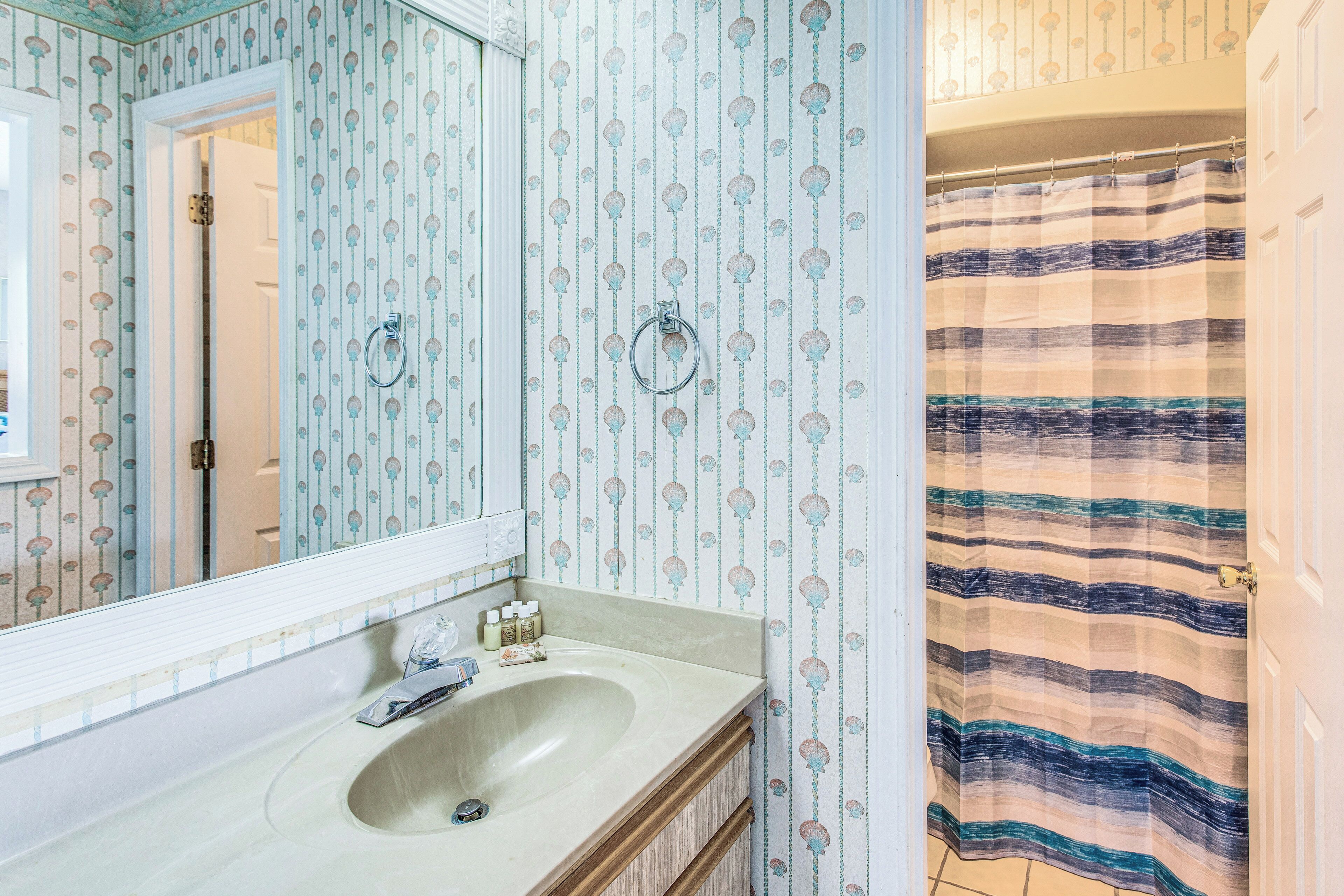 Een badkamer met een wastafel, spiegel en een douchegordijn met strepen.