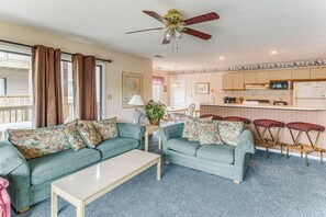 A living room with a ceiling fan, a sofa set, a dining table, and a kitchen area with bar stools. - Lake-view Balcony, Pool Access! Sunset Beach Condo (Sunset Beach)