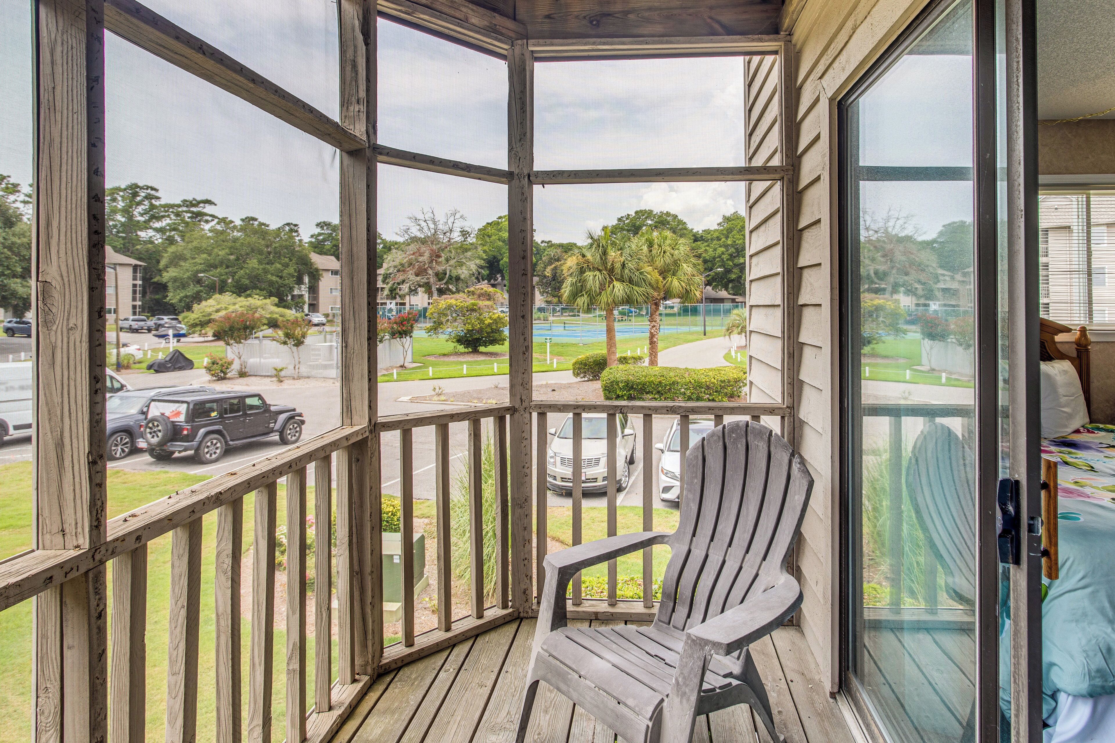 A wooden deck with a single Adirondack chair, overlooking a residential area with houses, a road, and a golf course.