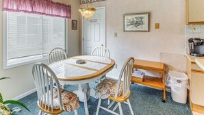 A dining area with a round table, chairs, a chandelier, a window with blinds, a door, and a kitchen area with appliances. - Lake-view Balcony, Pool Access! Sunset Beach Condo (Sunset Beach)