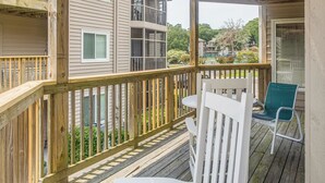A wooden deck with a white chair and a table, overlooking a residential area with multiple buildings and greenery. - Lake-view Balcony, Pool Access! Sunset Beach Condo (Sunset Beach)