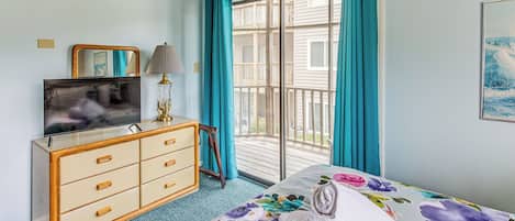 A bedroom with a bed, a dresser, a television, and a window with curtains.