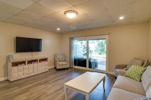 A living room with a television mounted on the wall, a sofa, a coffee table, and a sliding glass door leading to an outdoor area. - Private Patio, Yard! Townhome Near Pensacola Beach (Gulf Breeze)