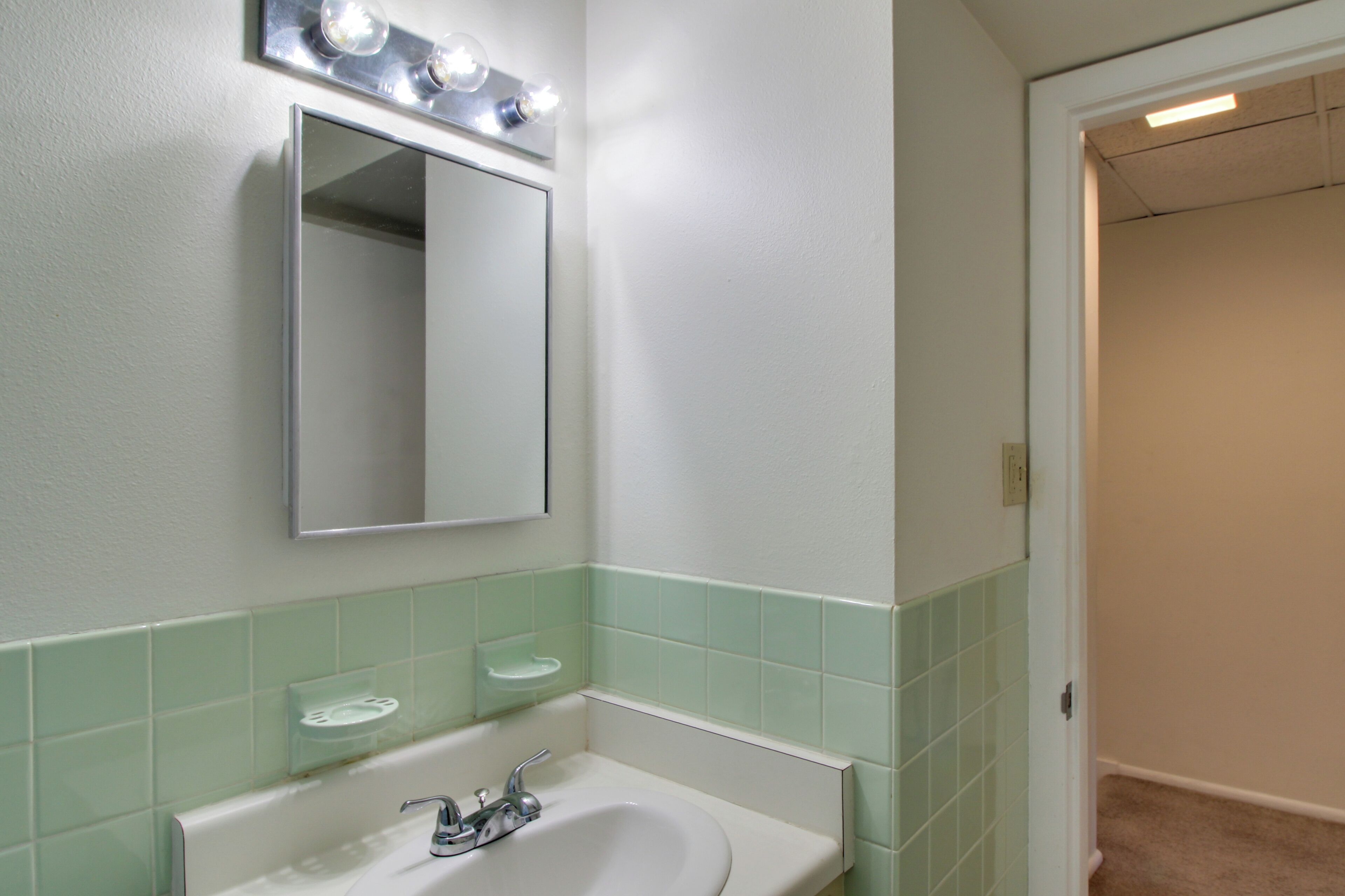 A bathroom with a white sink, a mirror, and a light fixture above it.