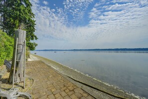 A calm lake with a wooden fence and a paved walkway along the shore. - Charming Waterfront Home With Mt Rainier View (Olympia)