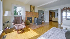 Een ruime woonkamer met een groot raam, een open haard, een schommelstoel en een keuken die zichtbaar is door een open deur.