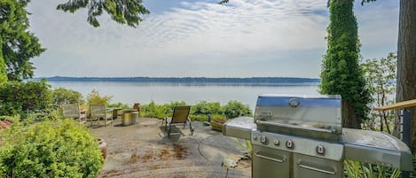 Un patio con una parrilla, mobiliario exterior y vistas a un lago.