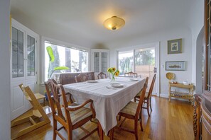 A dining room with a table set for four, wooden chairs, a vase with flowers, and a view of the outdoors through large windows. - Charming Waterfront Home With Mt Rainier View (Olympia)