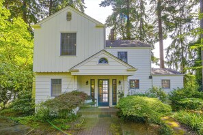 A two-story house with a front porch, surrounded by lush greenery and trees. - Charming Waterfront Home With Mt Rainier View (Olympia)