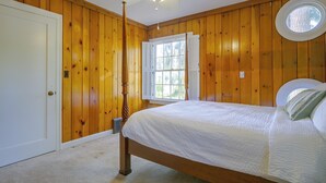 Een slaapkamer met houten wanden, een bed met een witte dekbedovertrek, een plafondventilator en een raam met luiken.