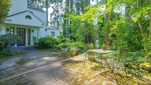 Een huis met een verharde oprit die leidt naar een overdekt terras met een tafel en stoelen.