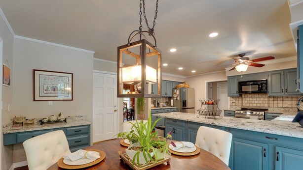 A dining area with a wooden table set for four, surrounded by blue cabinets, a ceiling fan, and a hanging light fixture. - Group Getaway w/ Private Yard in Marietta (Marietta)