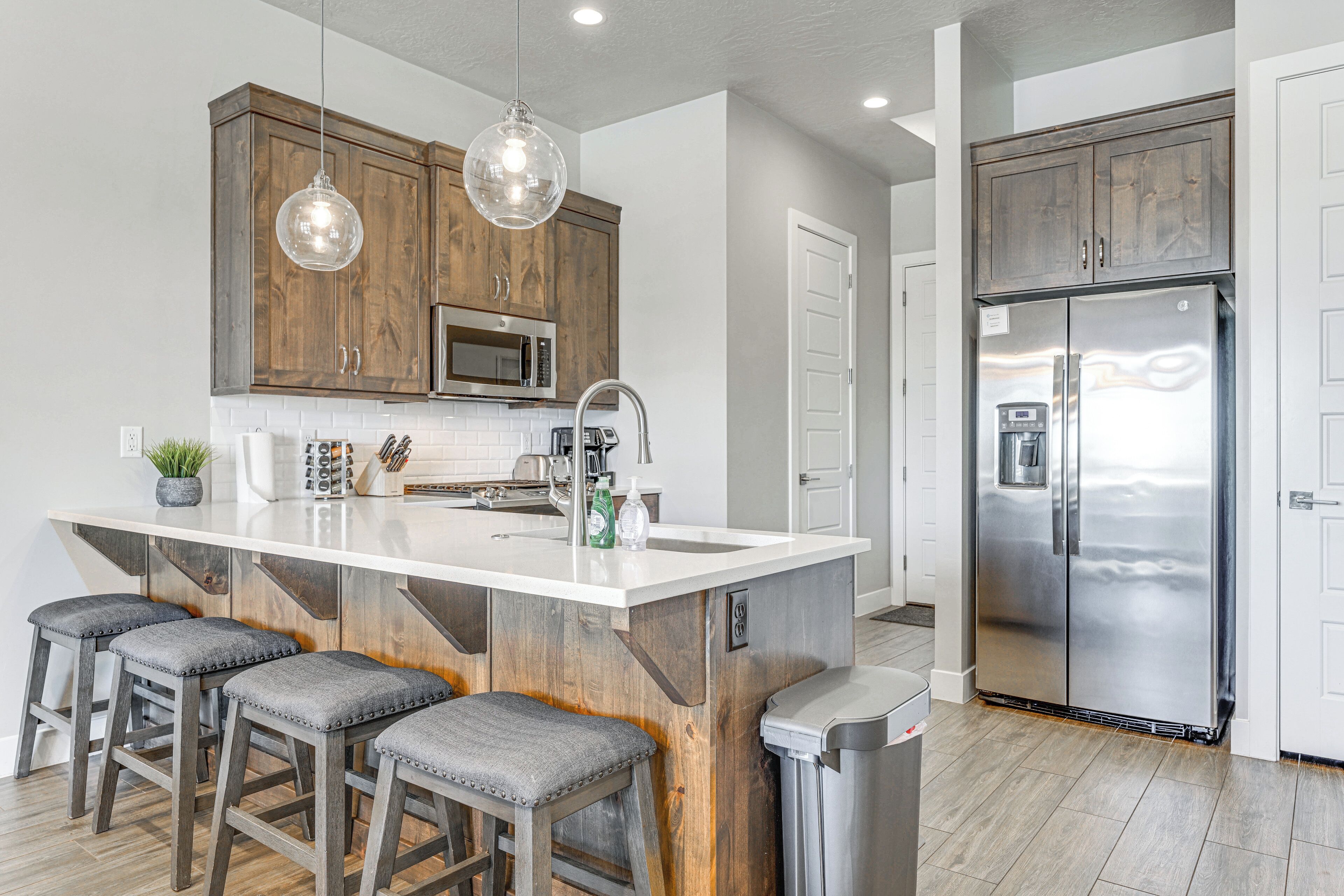 A modern kitchen with wooden cabinets, a stainless steel refrigerator, and a central island with bar stools.