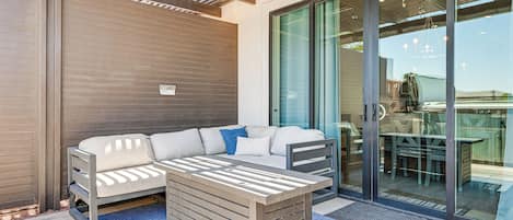 An outdoor seating area with a sofa and a table, a sliding glass door leading to a patio, and a ceiling with wooden beams.