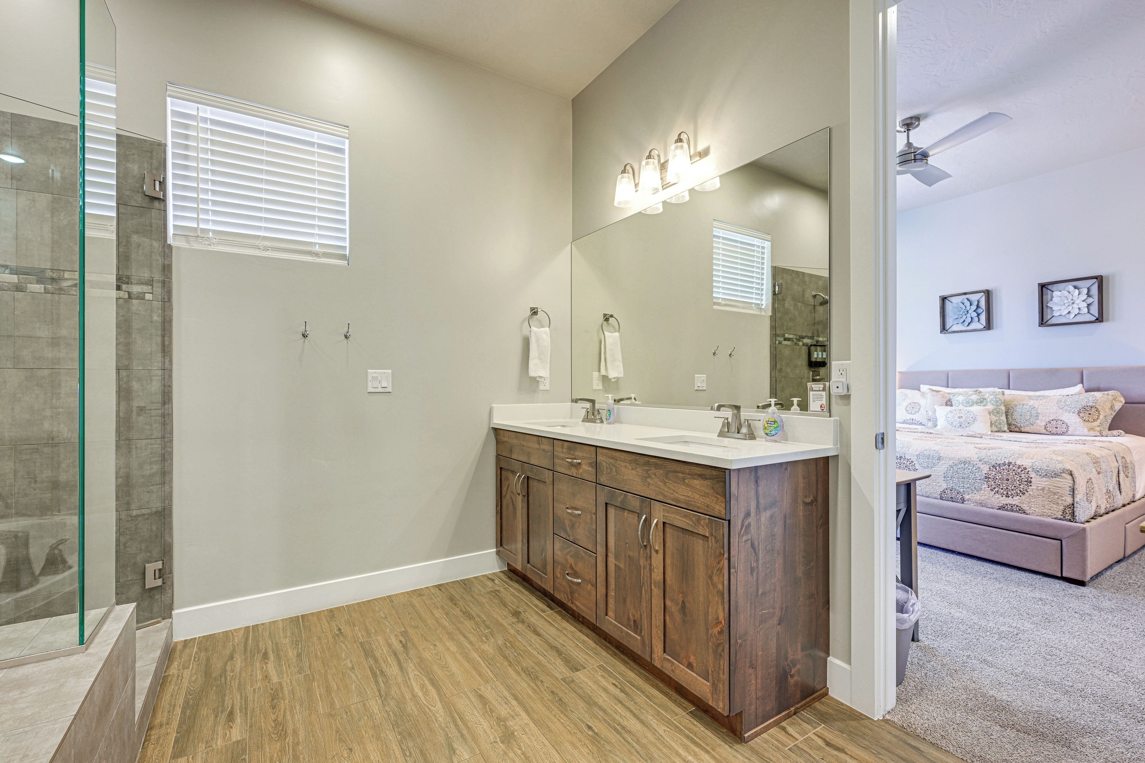 Un baño moderno con cabina de ducha de vidrio, tocador de madera y un espejo grande con luces.