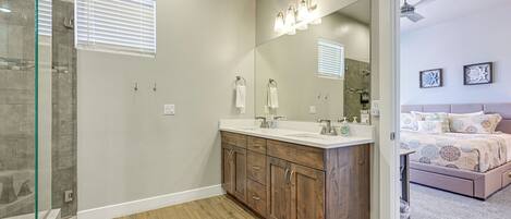 A modern bathroom with a glass shower enclosure, wooden vanity, and a large mirror with lights.