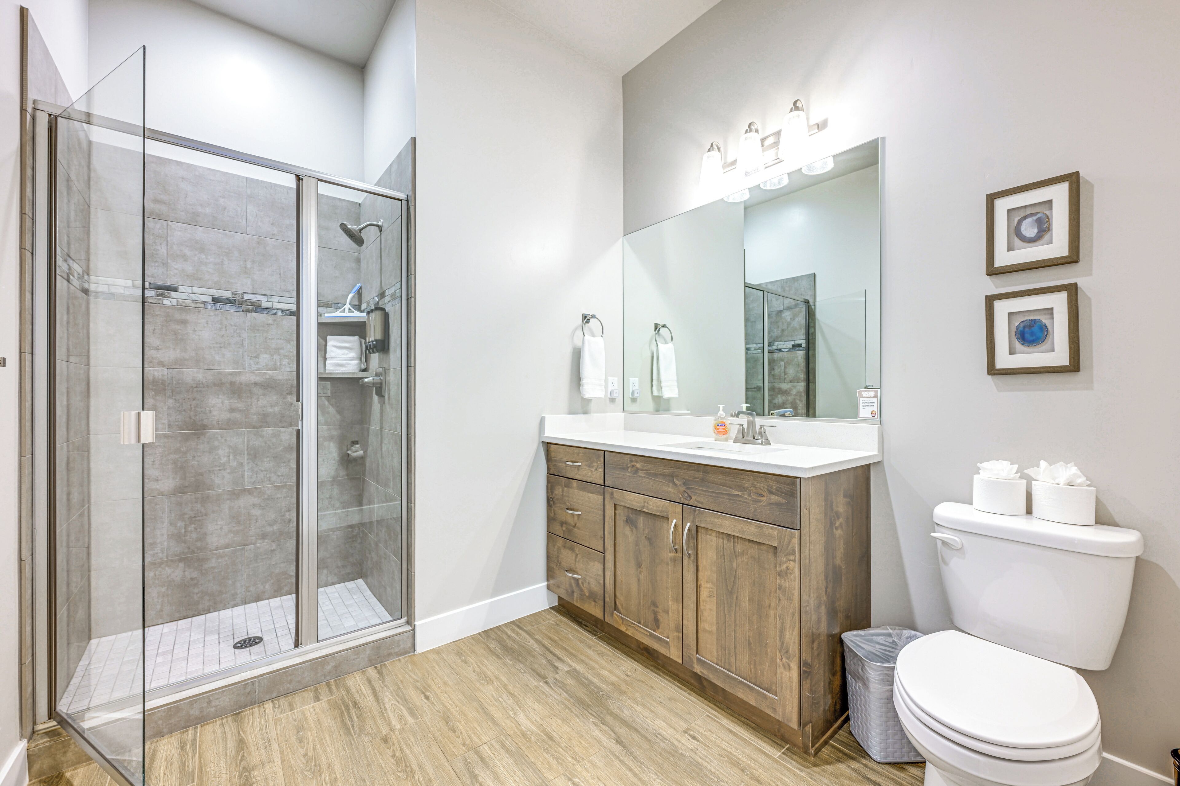 A modern bathroom with a glass-enclosed shower, wooden vanity, and a large mirror with lights.