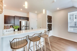 A modern kitchen with a stainless steel refrigerator, dark wooden cabinets, and a white countertop. There are two bar stools with metal frames and wooden seats. - Walk to Cleveland Clinic! Contemporary Townhome (Cleveland)