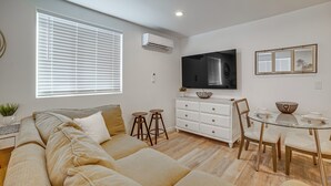 Ein modernes Wohnzimmer mit einer Couch, einem Esstisch mit Stühlen, einem flachbildfernseher an der Wand und einem Fenster mit Jalousien.