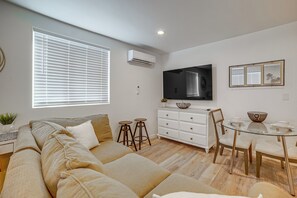 Ein modernes Wohnzimmer mit einer Couch, einem Esstisch mit Stühlen, einem flachbildfernseher an der Wand und einem Fenster mit Jalousien.
