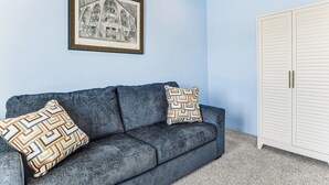 A room with a blue wall, a framed black and white drawing, a dark blue sofa with patterned cushions, and a white closet with horizontal lines. - 7 Mi to Saguaro Natl Park! Mtn-view Haven w/ Pool (Tucson)
