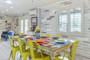 A dining area with a brick wall, a large window with blinds, and a table set with colorful plates and a vase of flowers. - 7 Mi to Saguaro Natl Park! Mtn-view Haven w/ Pool (Tucson)