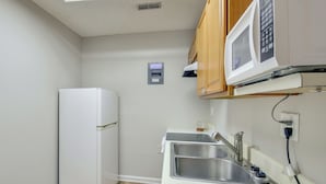 Uma cozinha compacta com micro-ondas integrado, uma pia de aço inoxidável e uma geladeira pequena.