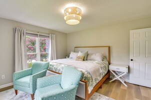 Un dormitorio con cama, dos sillas, una ventana con cortinas, una lámpara de techo y una puerta.