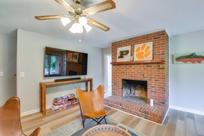 Una sala de estar con chimenea, ventilador de techo y televisión montada en la pared.