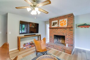 Una sala de estar con chimenea, ventilador de techo y televisión montada en la pared.