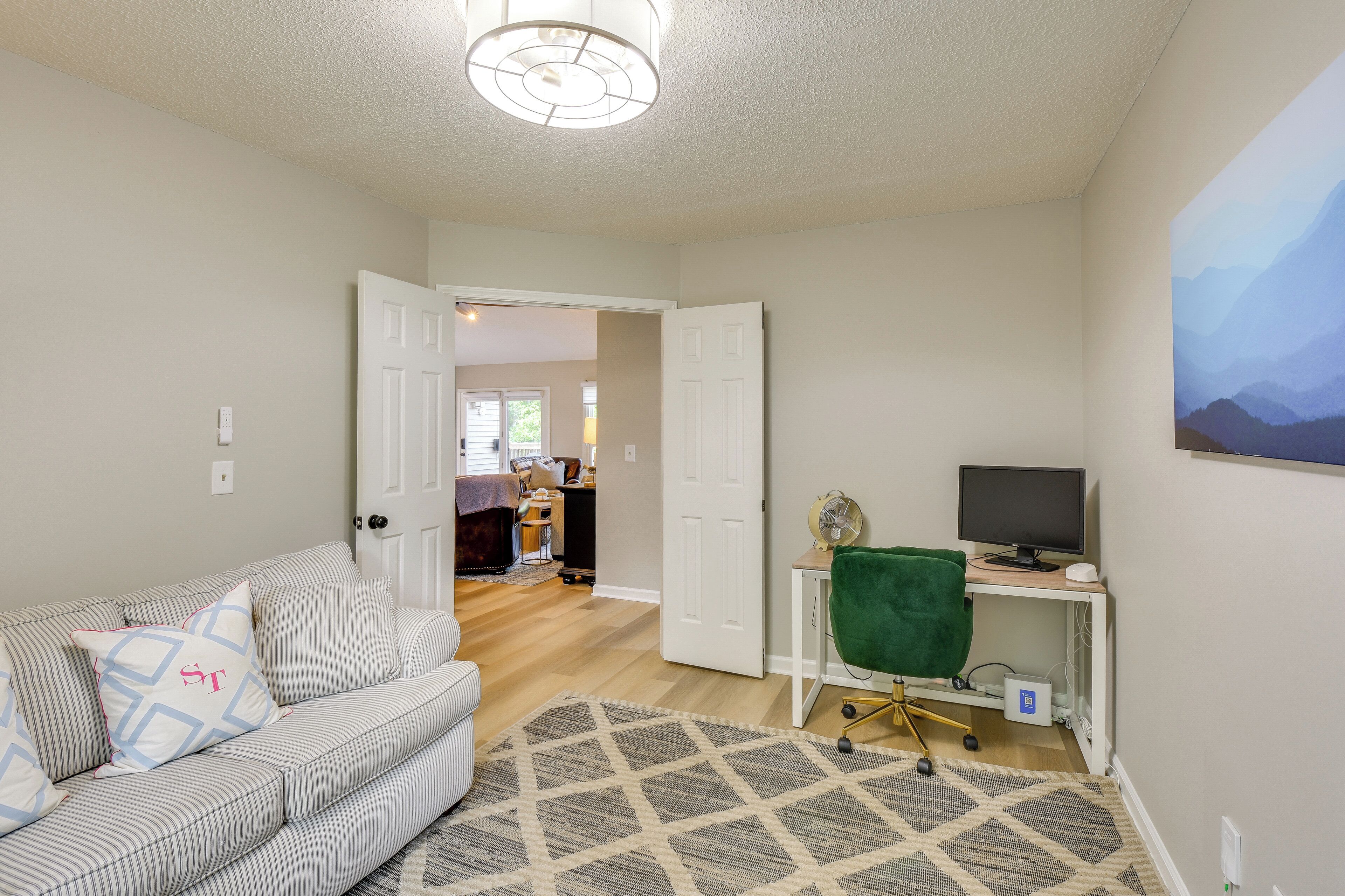 A living room with a sofa, a desk with a computer, a green chair, and a painting on the wall.