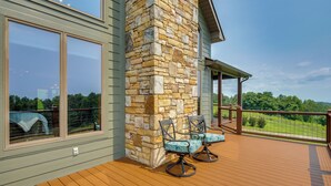 Una terraza de madera con mobiliario exterior, un pilar de piedra y vistas a un paisaje verde.