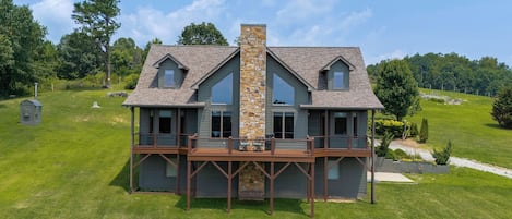 Une maison à deux étages avec une cheminée en pierre, une terrasse et un grand porche à l’avant.