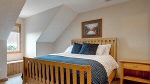 Un dormitorio con techo inclinado, estructura de cama de madera, mesita de noche y un cuadro enmarcado en la pared.