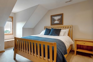 Ein Schlafzimmer mit schräg versiegelter Decke, einem hölzernen Bettgestell, einem Nachttisch und einem gerahmten Bild an der Wand.