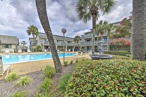 A pool area with lounge chairs and palm trees, surrounded by a building with balconies. - Pool Days + Beach Strolls! Ground-floor PCB Condo (Panama City Beach)