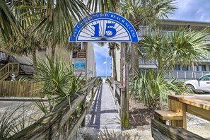 Ein hölzerner Steg führt zu einem Zugang zur Strandbucht, mit einem Schild, auf dem '15 Öffentlicher Strandzugang' steht.