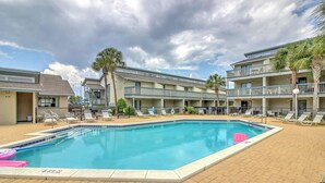 Piscina com espreguiçadeiras e palmeiras, cercada por um edifício com varandas.