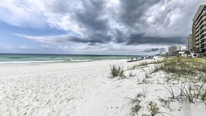 Uma praia com areal, céu nublado e um edifício com várias varandas.