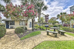 A courtyard with a paved walkway, stone benches, and flowering trees. - Pool Days + Beach Strolls! Ground-floor PCB Condo (Panama City Beach)