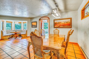 Un comedor con mesa y sillas de madera, un banco con cojines y vistas por las ventanas.