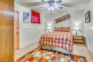 Un dormitorio con cama, dos lámparas de noche, ventilador de techo, cortina roja, un cartel en la pared y una decoración con trineo de madera.
