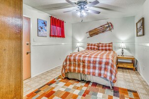 Un dormitorio con cama, dos lámparas de noche, ventilador de techo, cortina roja, un cartel en la pared y una decoración con trineo de madera.