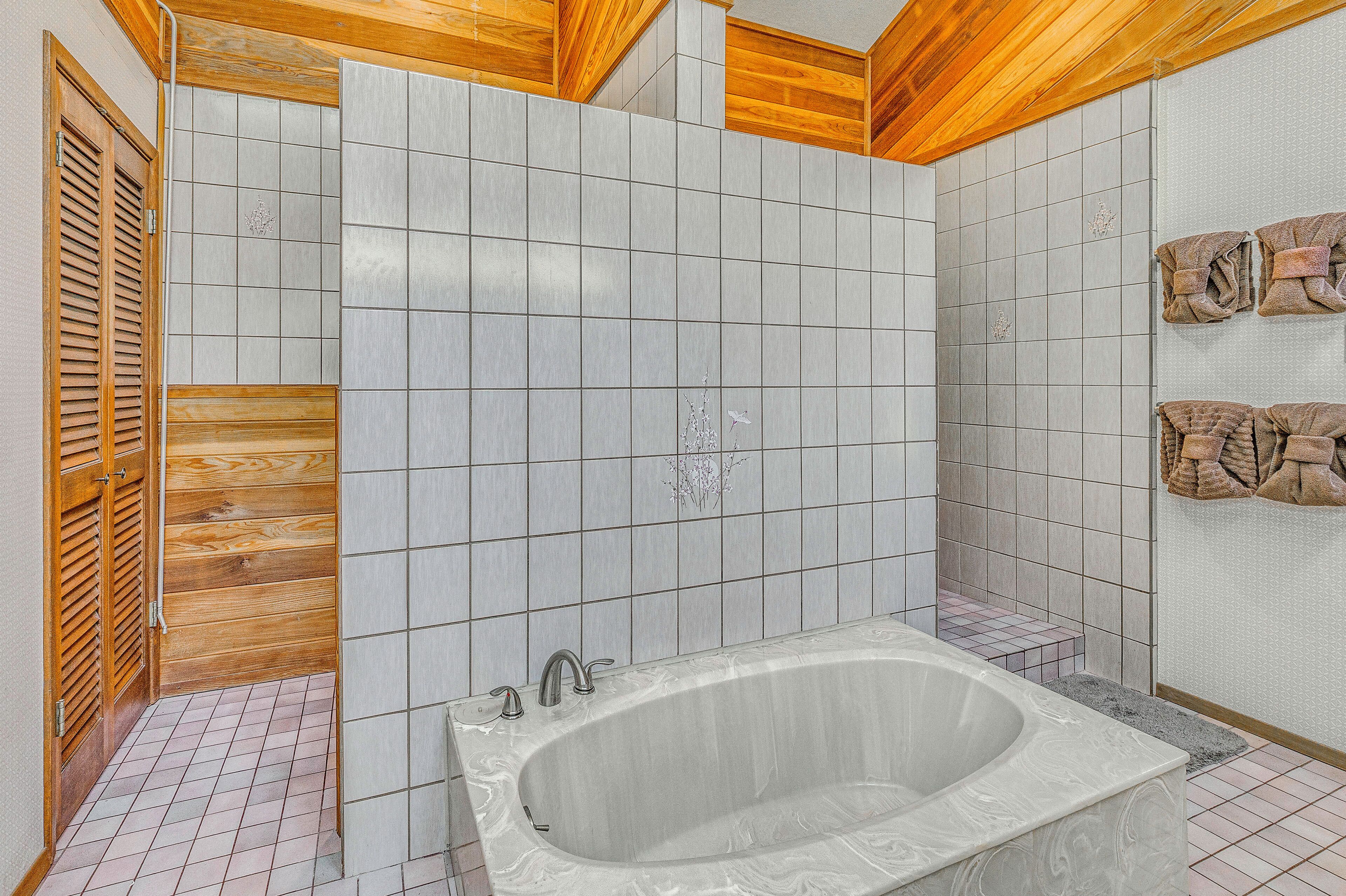 Baño con bañera, paredes de azulejos, vigas de madera en el techo y un perchero con toallas.