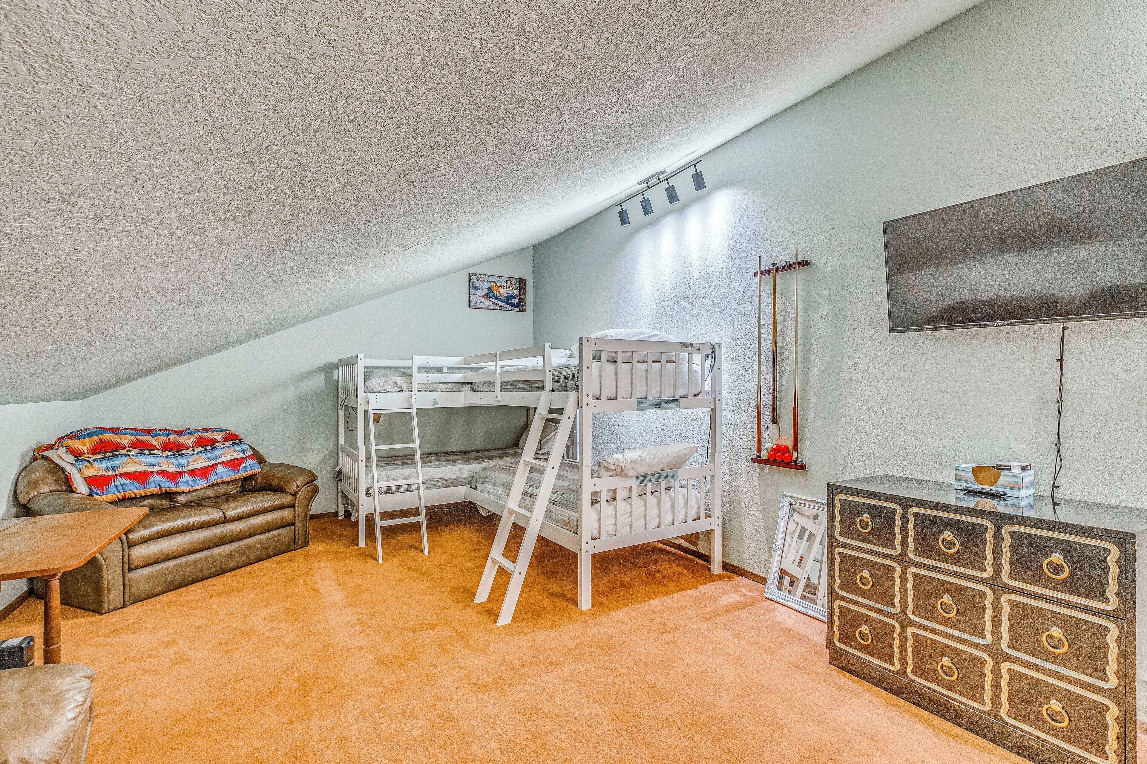 Habitación con literas, un sofá, un aparador y televisor montado en la pared.